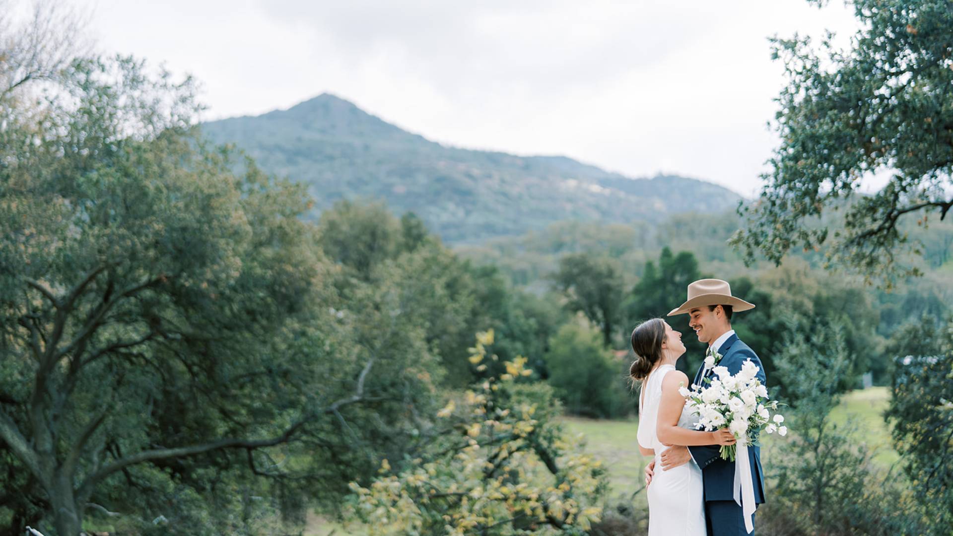 Couple embracing outdoors with mountain backdrop.