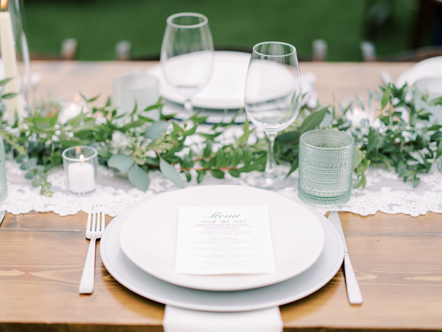 Elegant table setting with white plates, greenery, and glassware.