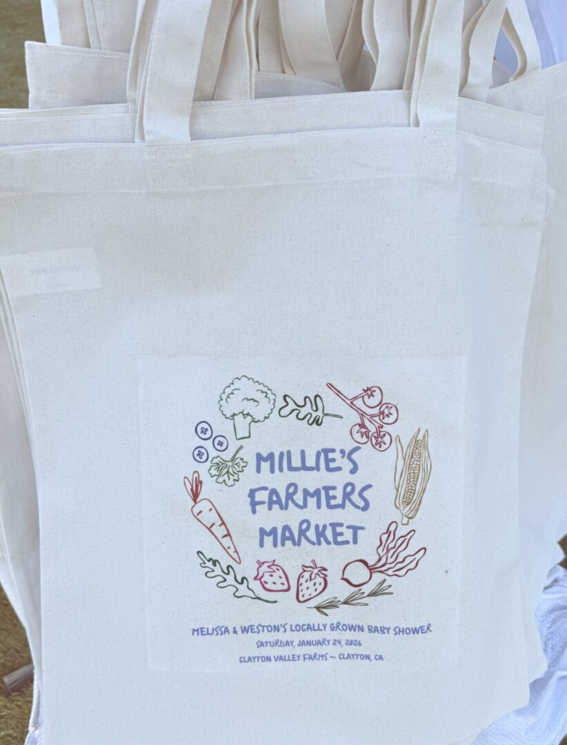 A white tote bag with "Milley's Farmers Market" and floral designs.