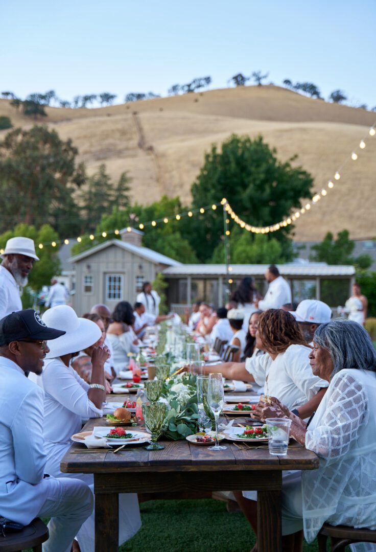 Outdoor gathering with people dining under string lights in a rural setting.