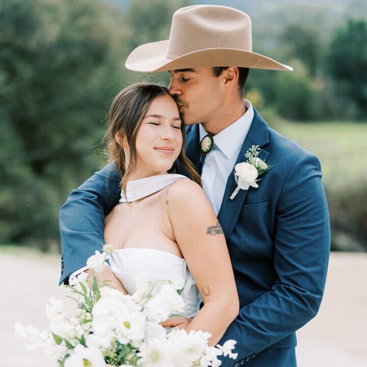 A groom tenderly embracing his bride outdoors.
