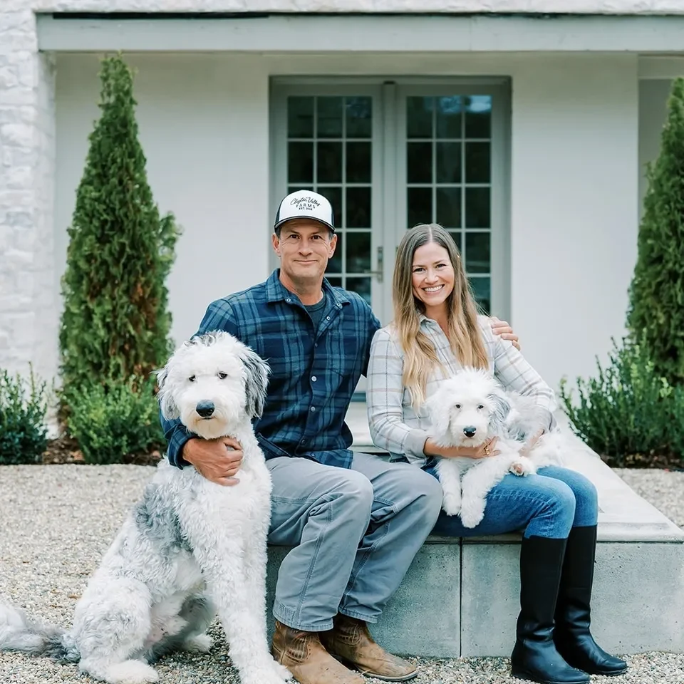 Couple sitting outdoors with two white dogs on a sunny day.
